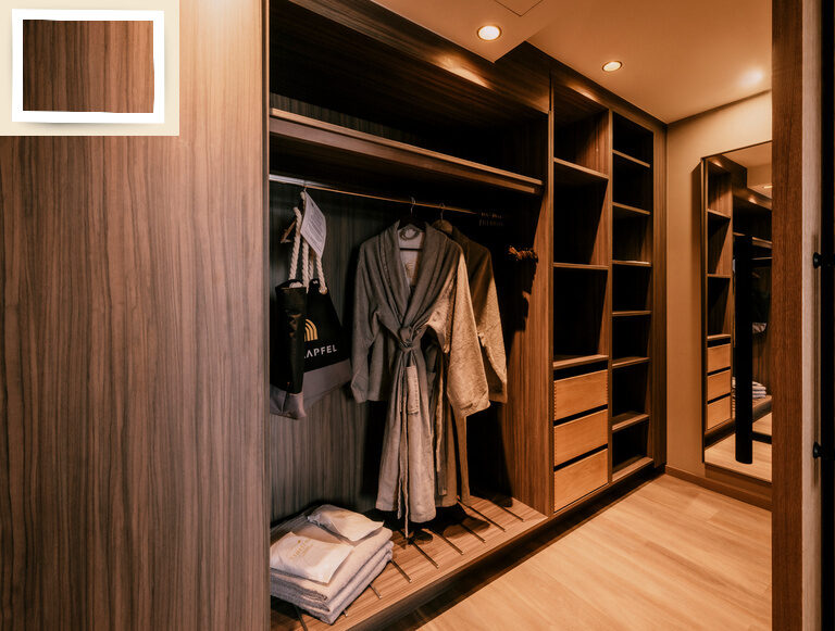 Ein großzügiger begehbarer Kleiderschrank mit Holzoptik und hängender Kleidung darin in der Suite Goldrenette Thermenhotel Holzapfel.
